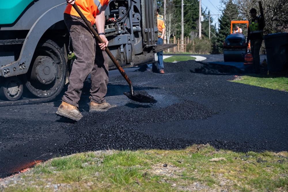 Construction,worker,shoveling,freshly,laid,asphalt,on,transition,between,street
